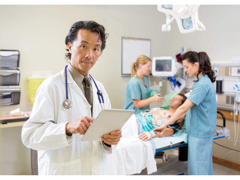 Doctor using tablet while nurses treating patient